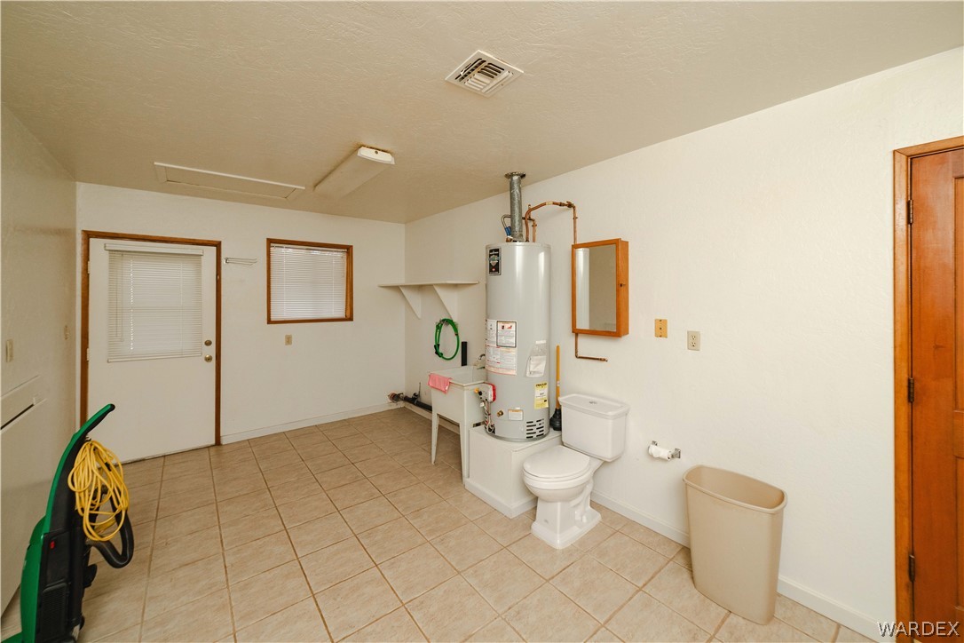 2100 East Valley View Road Kingman, AZ 86409 - Photo 33 of 53 Utility room featuring tiled flooring, a built-in utility sink, a water heater, a toilet, and an exterior access door with a window