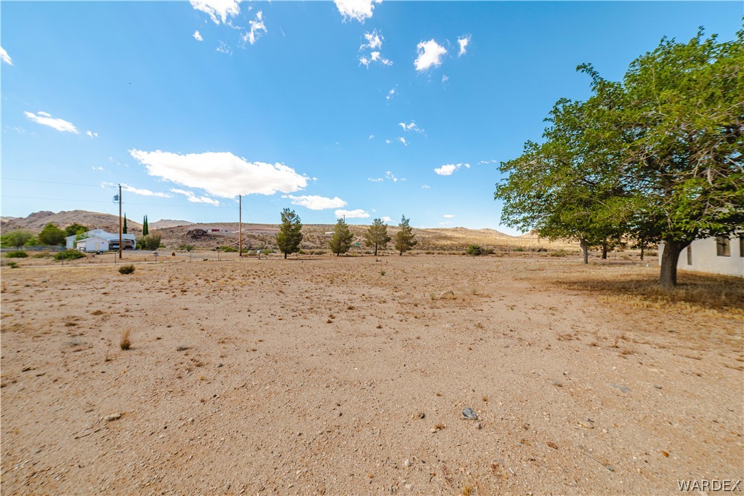 2100 East Valley View Road Kingman, AZ 86409 - Photo 50 of 53 Expansive undeveloped land parcel featuring mature trees, a distant single-story structure, and a mountainous backdrop under a clear sky with scattered clouds