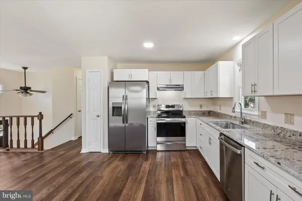 a kitchen with granite countertop a refrigerator oven a sink dishwasher and white cabinets with wooden floor