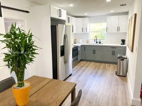 a kitchen with stainless steel appliances a refrigerator a sink a wooden floor cabinets and a potted plant