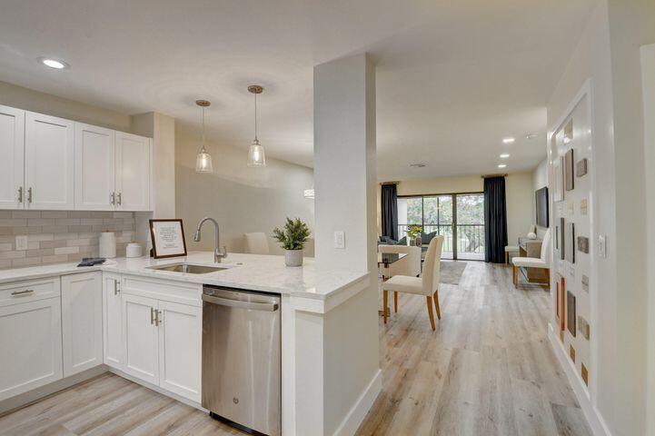a open kitchen with a sink dishwasher a stove and white cabinets with wooden floor