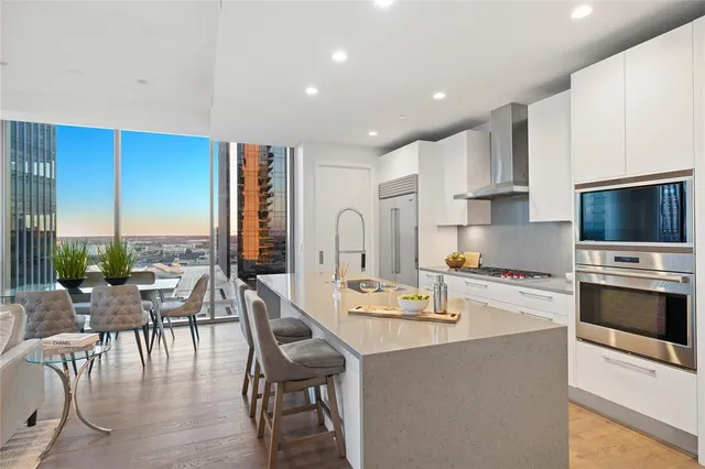 a kitchen with stainless steel appliances granite countertop a stove top oven a sink a dining table and chairs with wooden floor