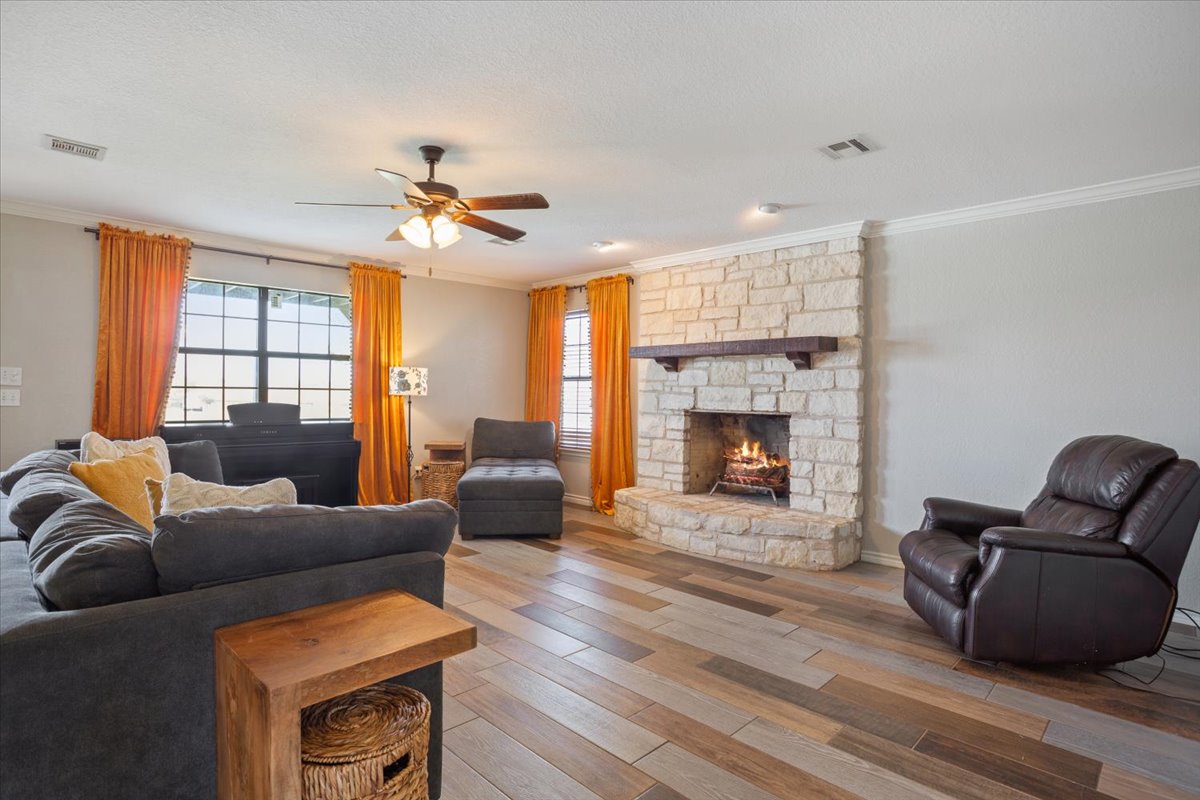 8600 Five Wells Road Rogers, TX 76569 - Photo 14 of 40 Living room featuring wood finished floors, crown molding, a stone fireplace, and ceiling fan
