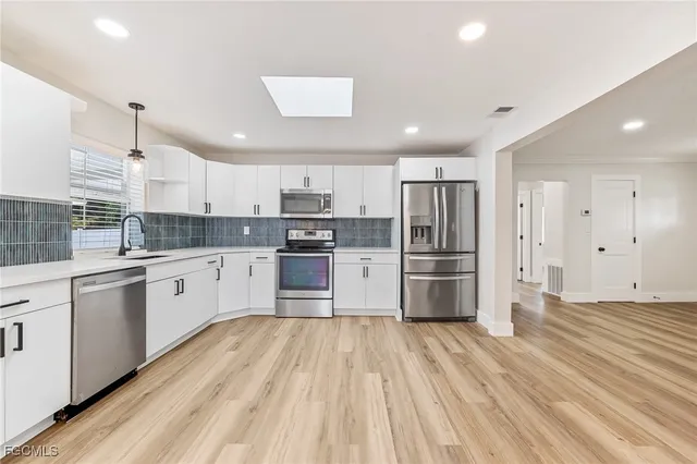 a large kitchen with stainless steel appliances sink a stove and white cabinets