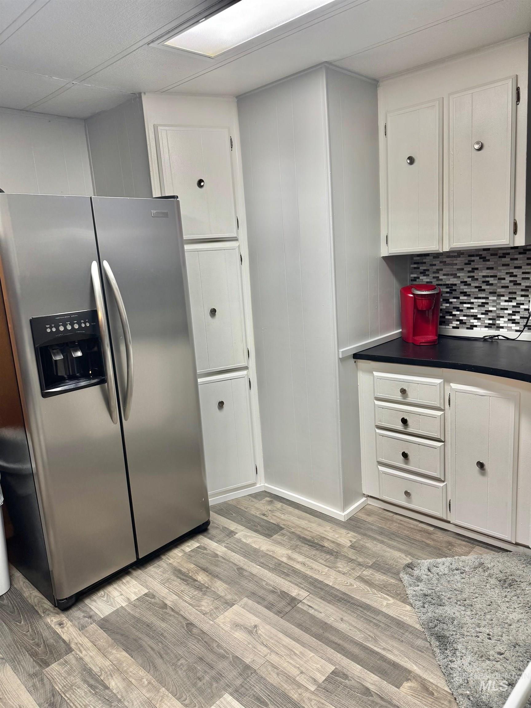 3181 West Alpine Street, Unit 22 Boise, ID 83705 - Photo 9 of 24 Kitchen with stainless steel fridge, white cabinets, light wood-style floors, dark countertops, and backsplash