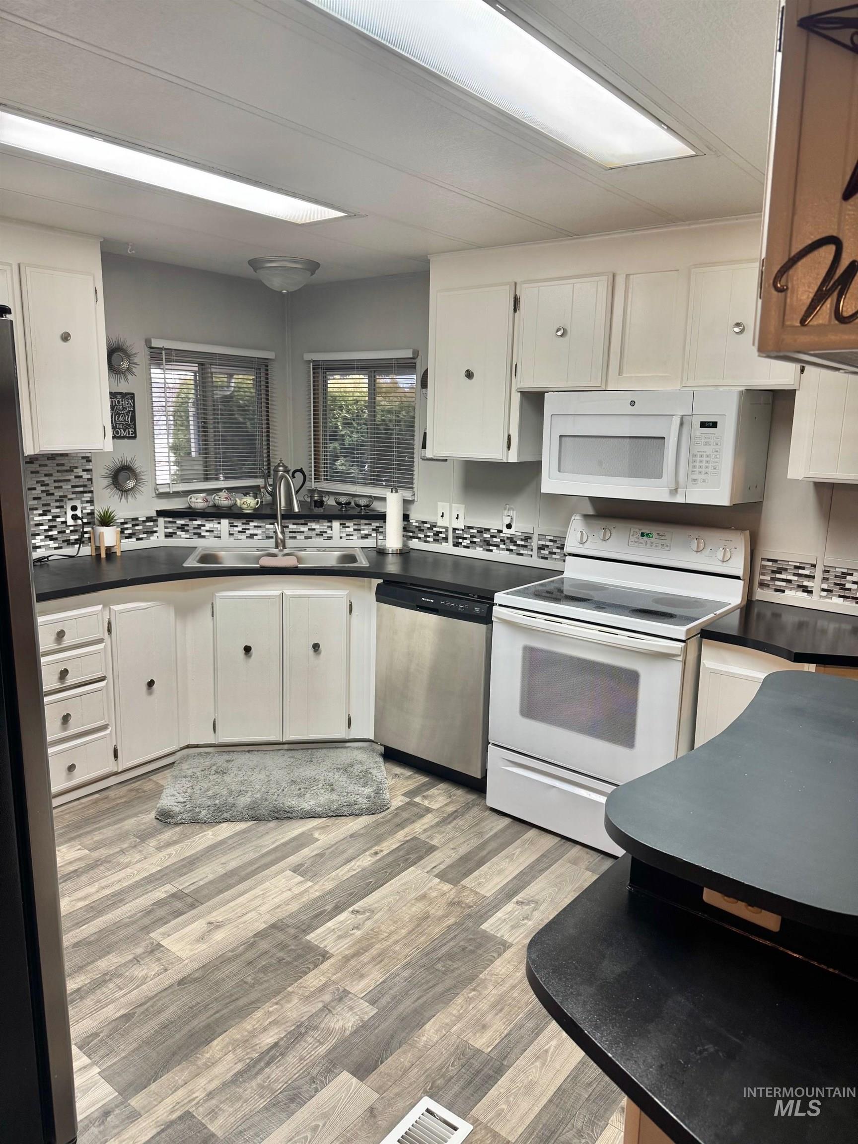 3181 West Alpine Street, Unit 22 Boise, ID 83705 - Photo 10 of 24 Kitchen with stainless steel appliances, white cabinetry, light wood finished floors, and dark countertops