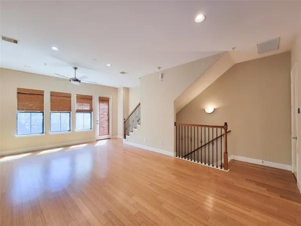 a view of an empty room with wooden floor and fan