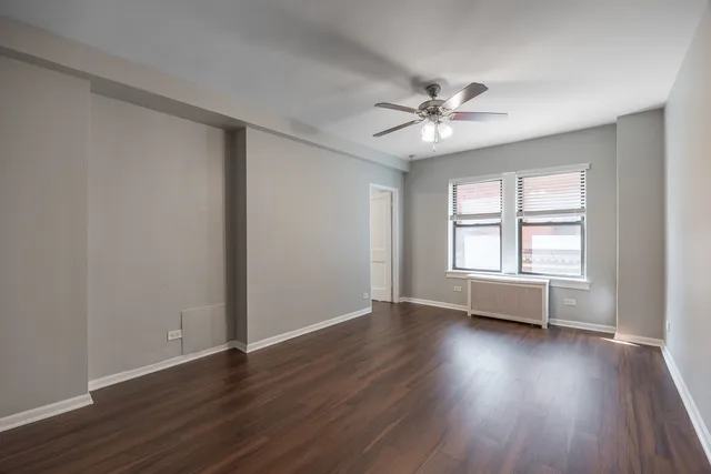an empty room with wooden floor window and ceiling fan