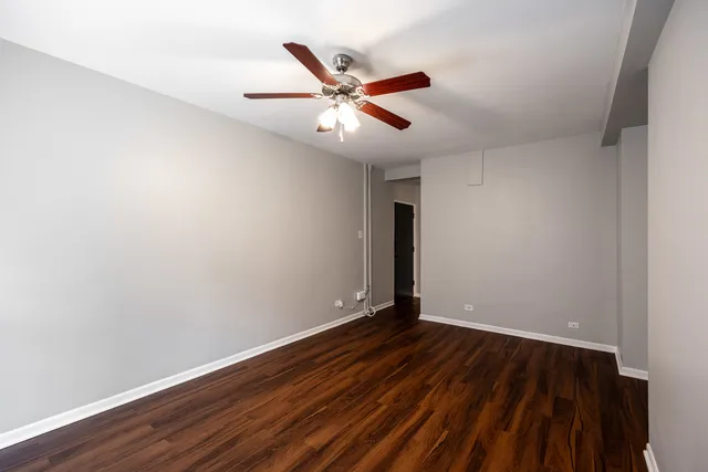 an empty room with wooden floor ceiling fan and window