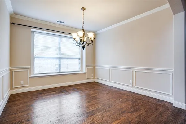 a view of an empty room with chandelier and wooden floor