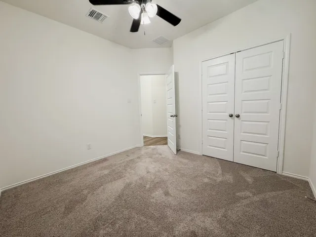 an empty room with a ceiling fan and carpet