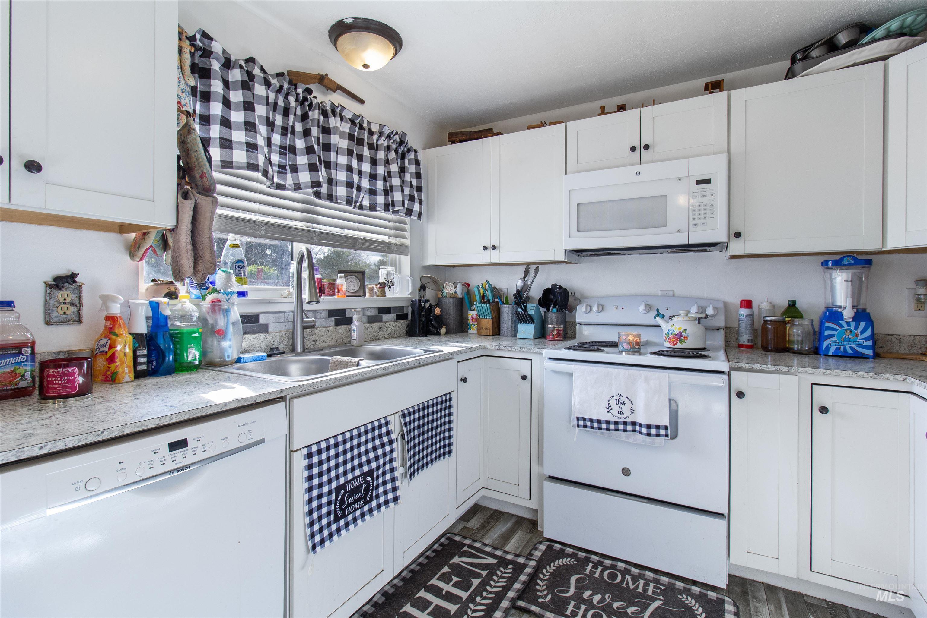 636 Main Street Hansen, ID 83334 - Photo 13 of 37 Kitchen featuring white cabinetry, light-colored countertops, a double basin sink with a high-arc faucet, a built-in microwave, and wood-finish flooring