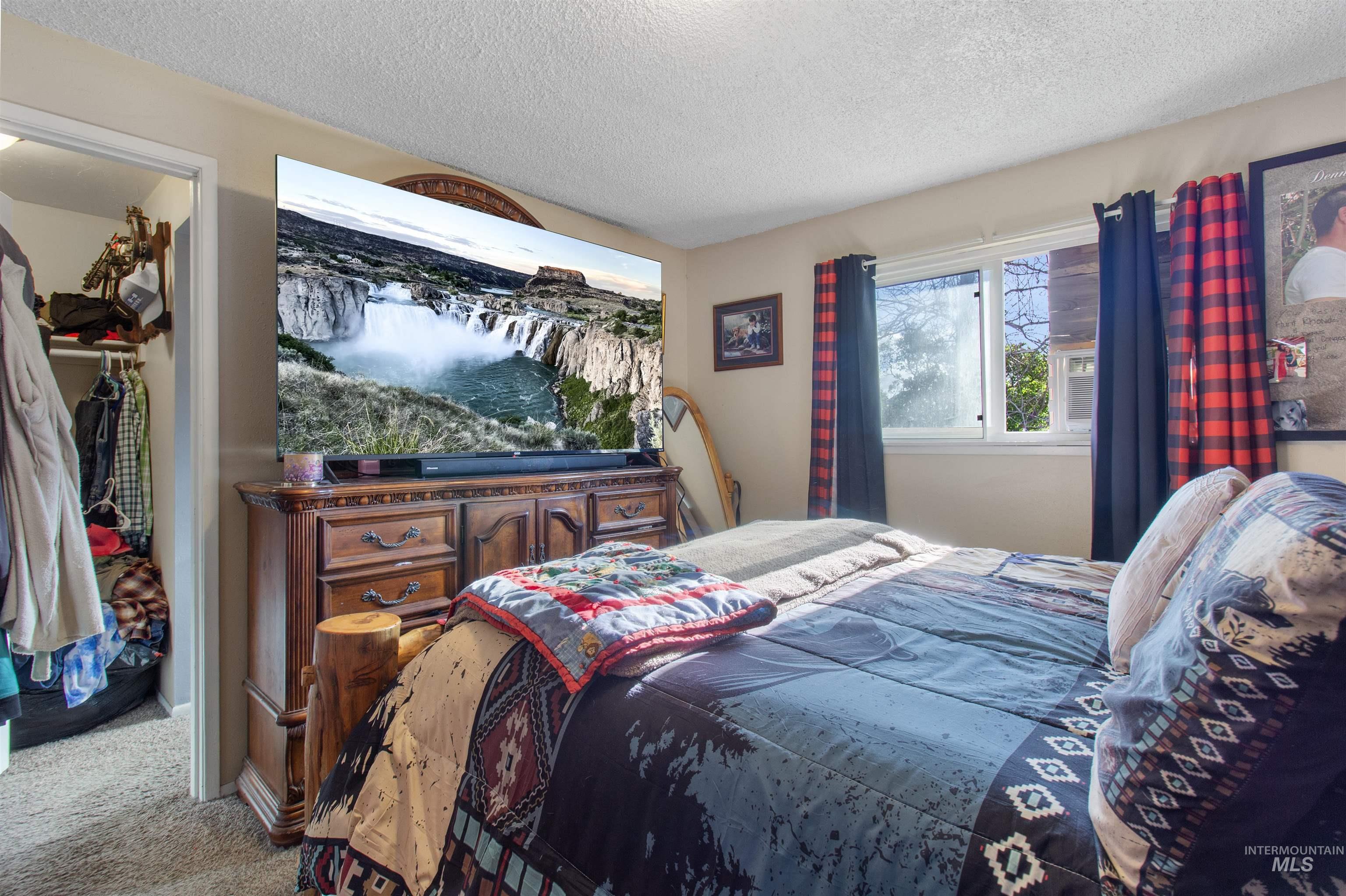 636 Main Street Hansen, ID 83334 - Photo 17 of 37 Carpeted bedroom featuring a large window with white trim, a built-in closet with shelving and hanging rods, and a textured ceiling