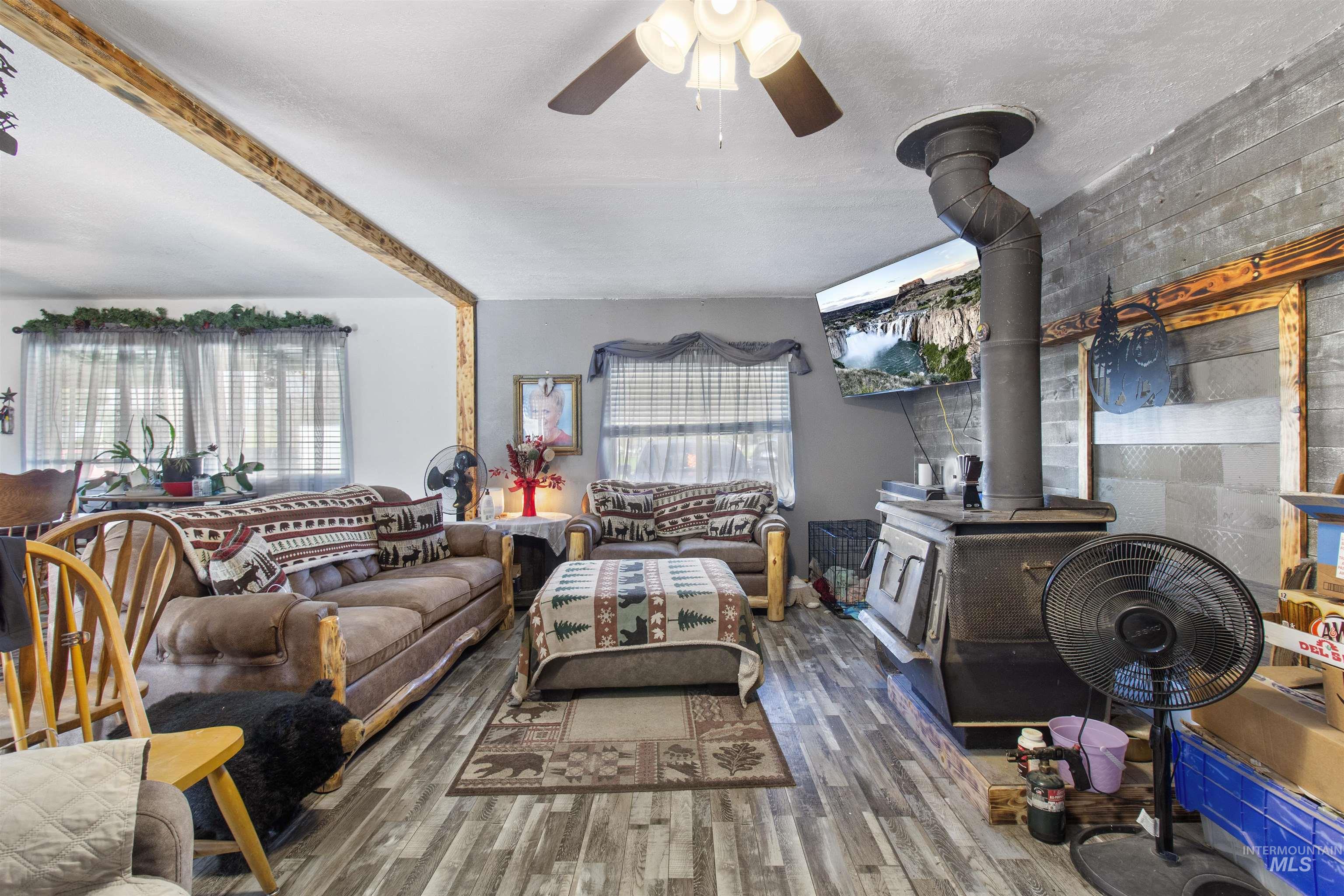 636 Main Street Hansen, ID 83334 - Photo 7 of 37 Living area featuring wood-finish flooring, a ceiling fan, and a wood-burning stove with a visible flue