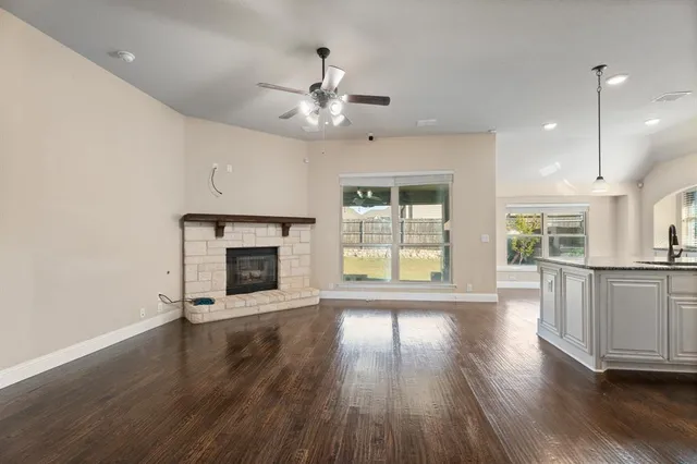 an empty room with wooden floor a ceiling fan a fireplace and windows