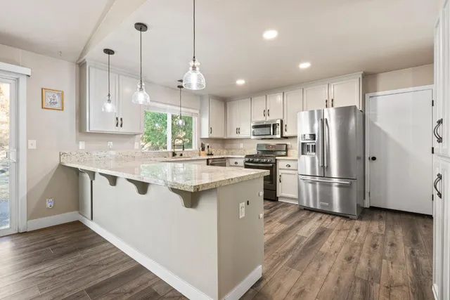 a kitchen with stainless steel appliances granite countertop a refrigerator a sink dishwasher a kitchen island with wooden floor and cabinets