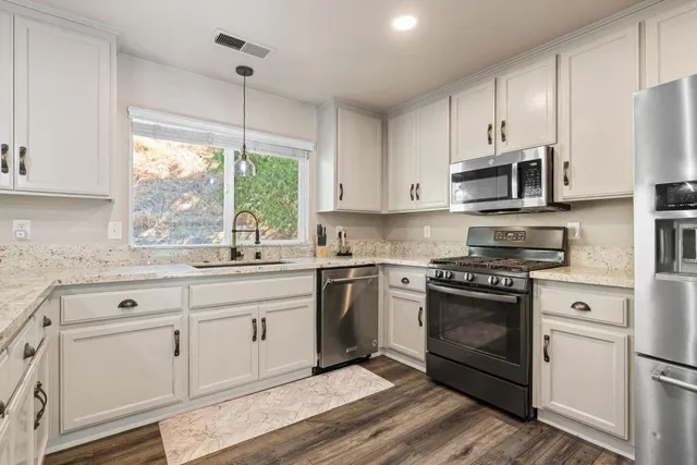 a kitchen with white cabinets appliances a sink and a window
