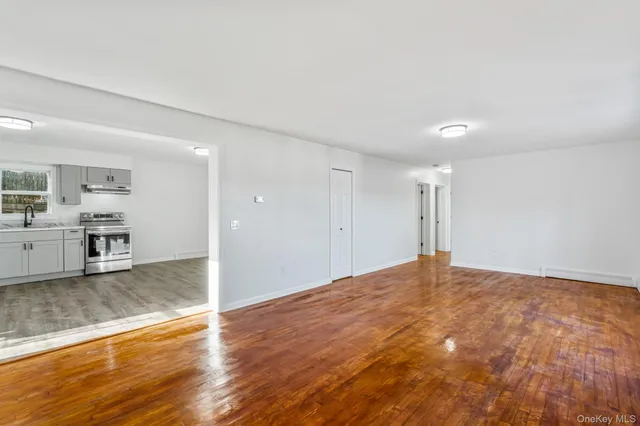 a view of an empty room with wooden floor and a kitchen