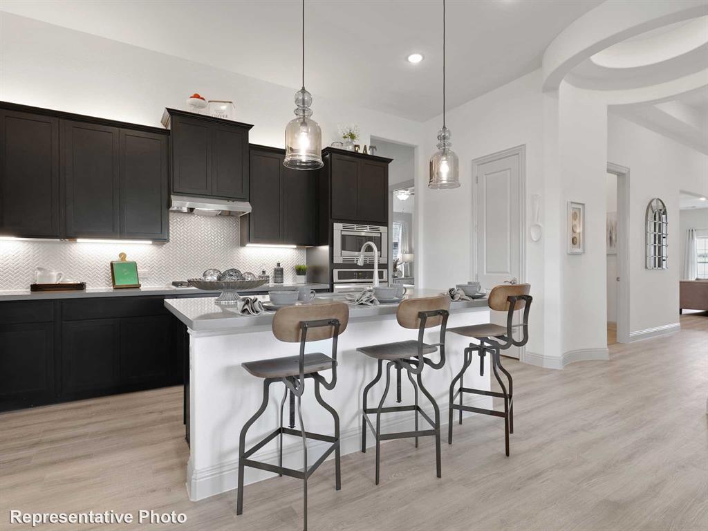 2204 Ridgecrest Lane Anna, TX 75409 - Photo 2 of 17 Kitchen island with a light-colored countertop and seating, illuminated by two pendant lights