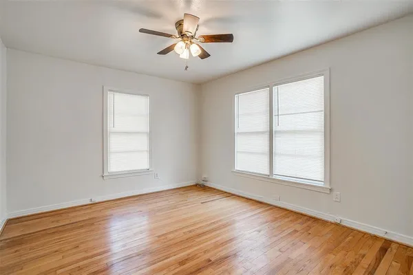 an empty room with wooden floor chandelier fan and windows
