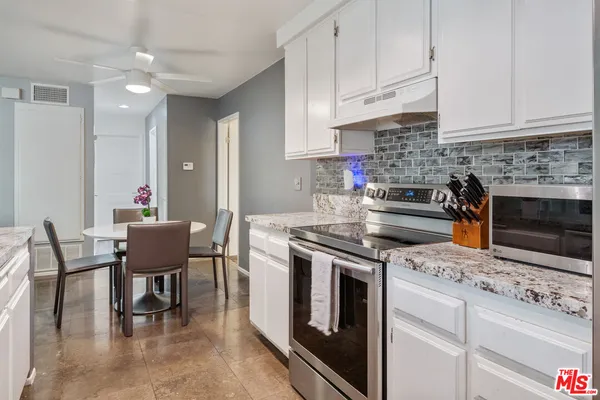 a kitchen with stainless steel appliances granite countertop a stove a sink a refrigerator a dining table and chairs