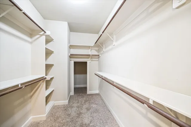 an empty room with chandelier fan and kitchen view