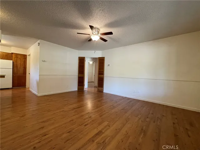 a view of an empty room with wooden floor and a ceiling fan
