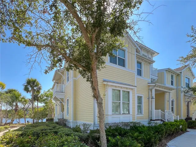 a view of a white house next to a yard with plants and trees