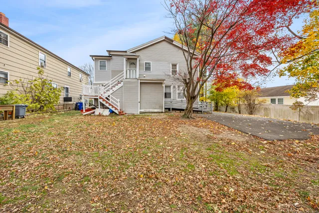 a view of a white house next to a road with large trees