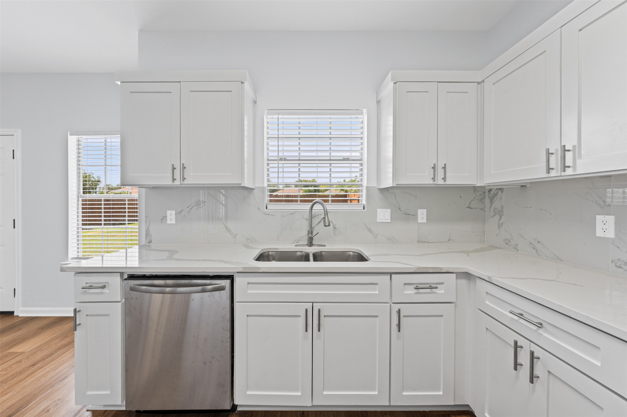243 Engineers Pass Jarrell, TX 76537 - Photo 11 of 40 Modern kitchen featuring white shaker-style cabinetry, a stainless steel double-basin sink, stainless steel dishwasher, and light-toned countertops with a matching backsplash