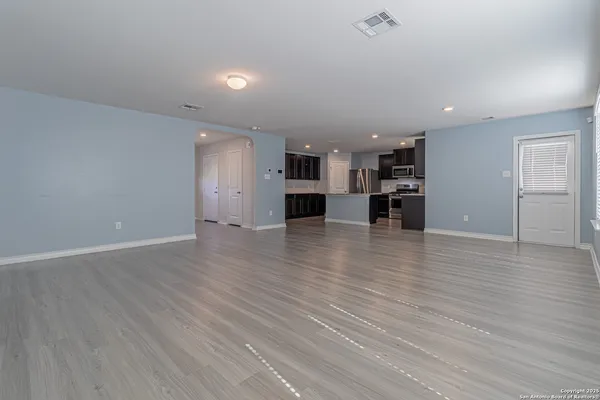 an empty room with wooden floor and a kitchen