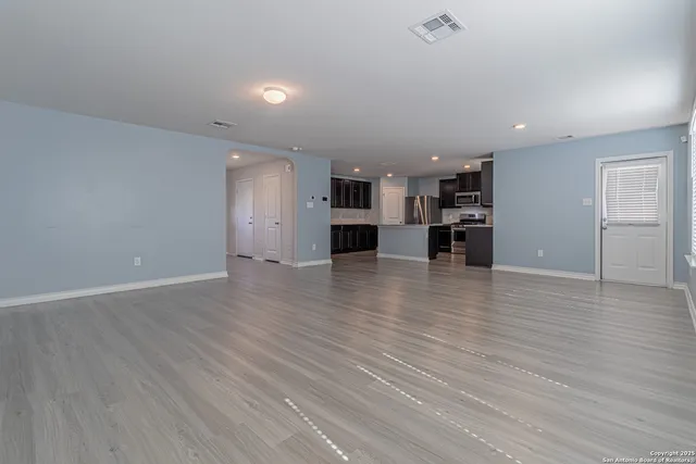 an empty room with wooden floor and a kitchen