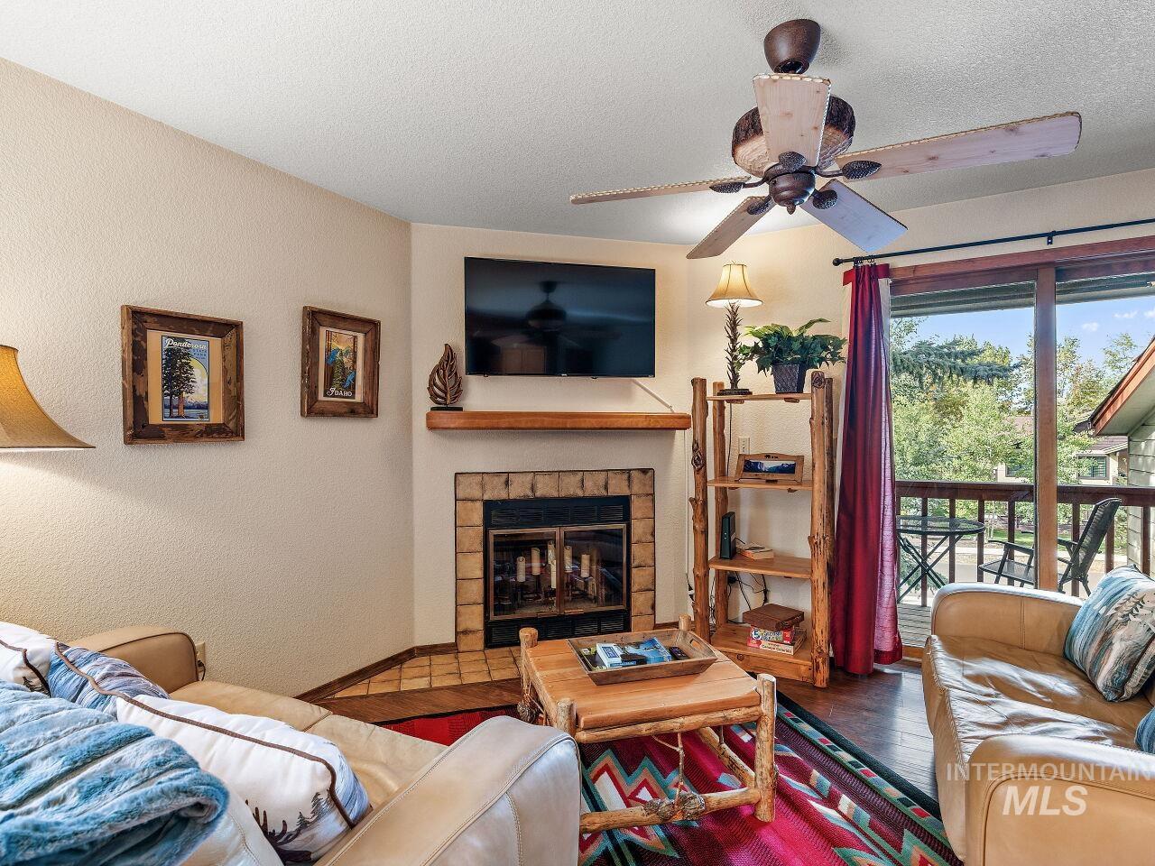 601 Hemlock Street, Unit 10 McCall, ID 83638 - Photo 13 of 43 Living room featuring a ceiling fan, wood finished floors, a glass covered fireplace, a textured ceiling, and a textured wall