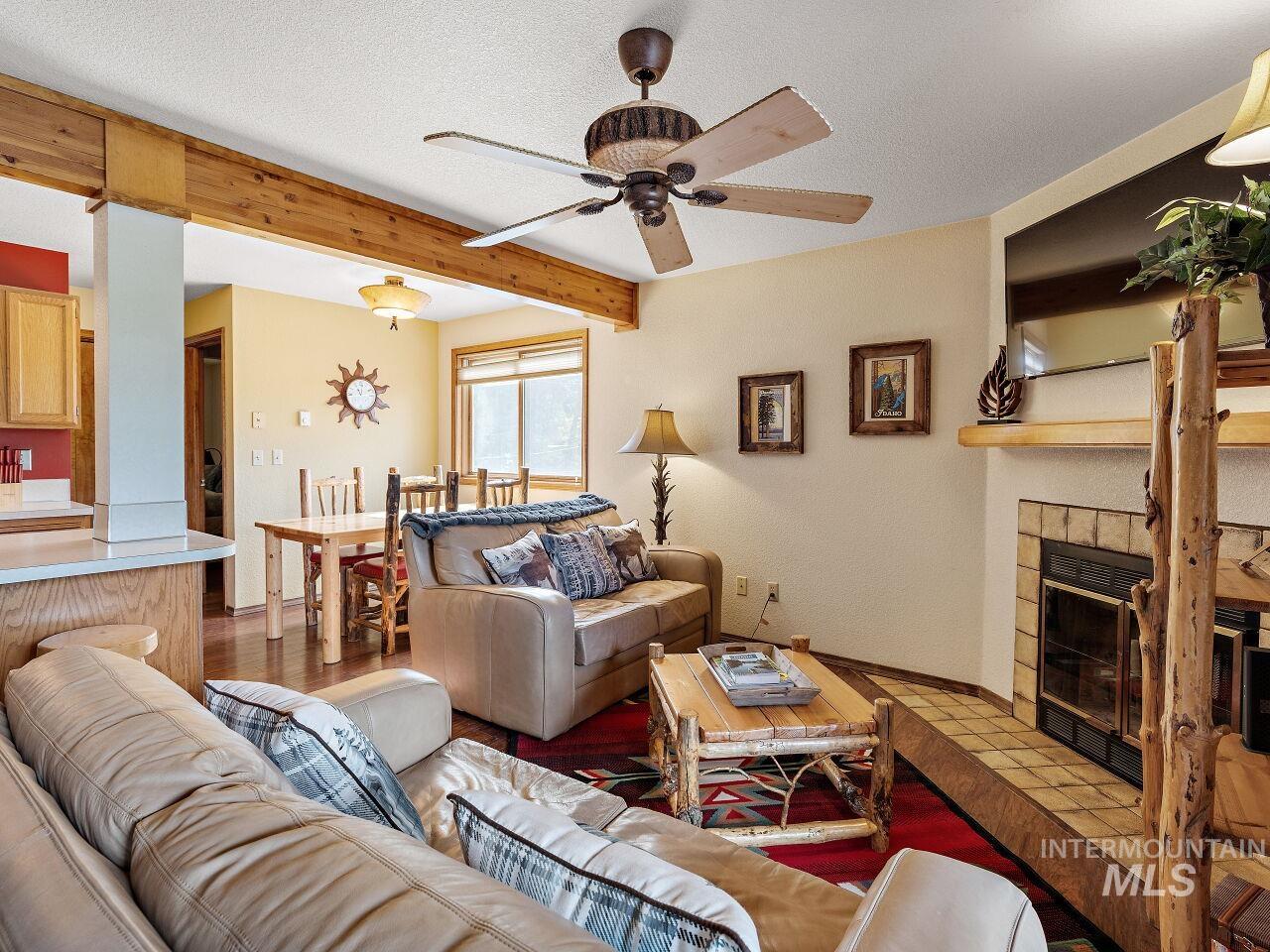 601 Hemlock Street, Unit 10 McCall, ID 83638 - Photo 10 of 43 Living room featuring ceiling fan, beam ceiling, a tiled fireplace, wood finished floors, and a textured ceiling
