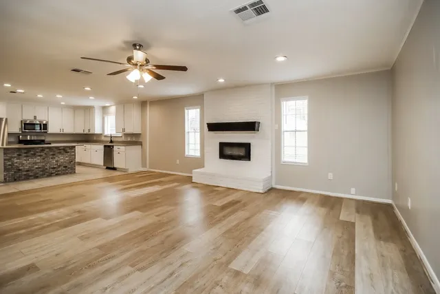 an empty room with wooden floor a ceiling fan and kitchen view