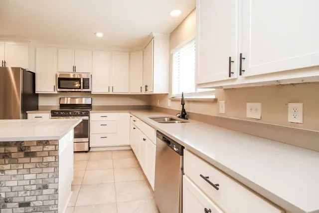 a kitchen with kitchen island granite countertop a sink appliances cabinets and a counter top space
