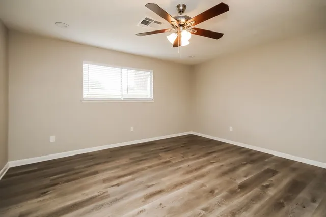 an empty room with wooden floor fan and windows
