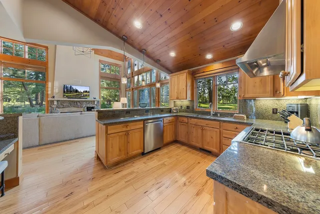 a kitchen with stainless steel appliances granite countertop wooden cabinets a stove a sink and a large window