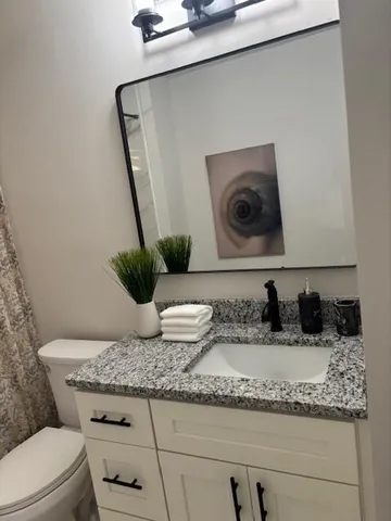 a bathroom with a granite countertop sink a toilet and a mirror