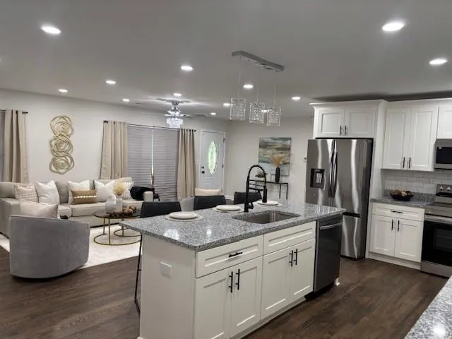 a kitchen with stainless steel appliances granite countertop a sink dishwasher a refrigerator and white cabinets with wooden floor