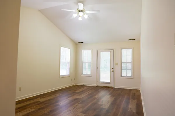 an empty room with wooden floor ceiling fan and windows