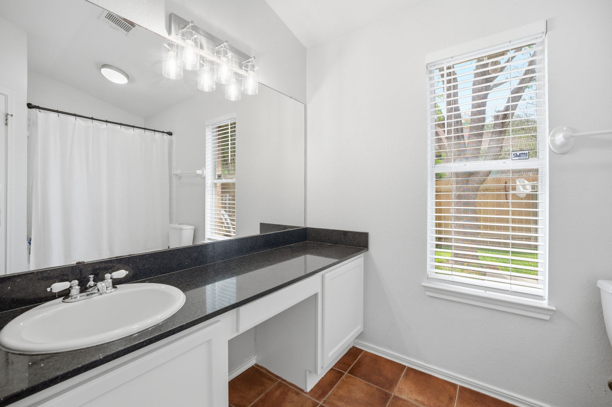 9024 Heiden Lane Austin, TX 78749 - Photo 17 of 28 Bathroom featuring a vanity with dark countertop and integrated sink, a large wall-mounted mirror, overhead vanity lighting, a window with blinds, and terracotta-toned floor tiles