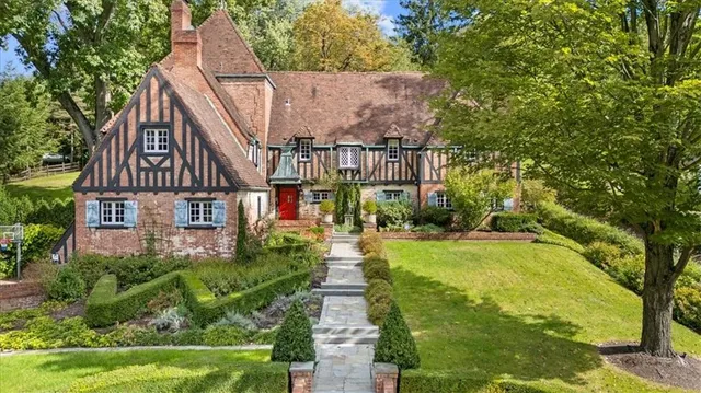 a view of a house with brick walls and a yard with plants and large trees