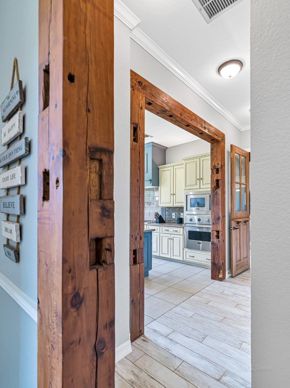 100 Pecan Grove Road Sealy, TX 77474 - Photo 14 of 48 This photo showcases a stylish interior with a staircase featuring decorative wrought iron balusters and dark wood steps. Adjacent is a hallway leading to a cozy living space with wooden floors and exposed ceiling beams, creating a warm and inviting atmosphere.