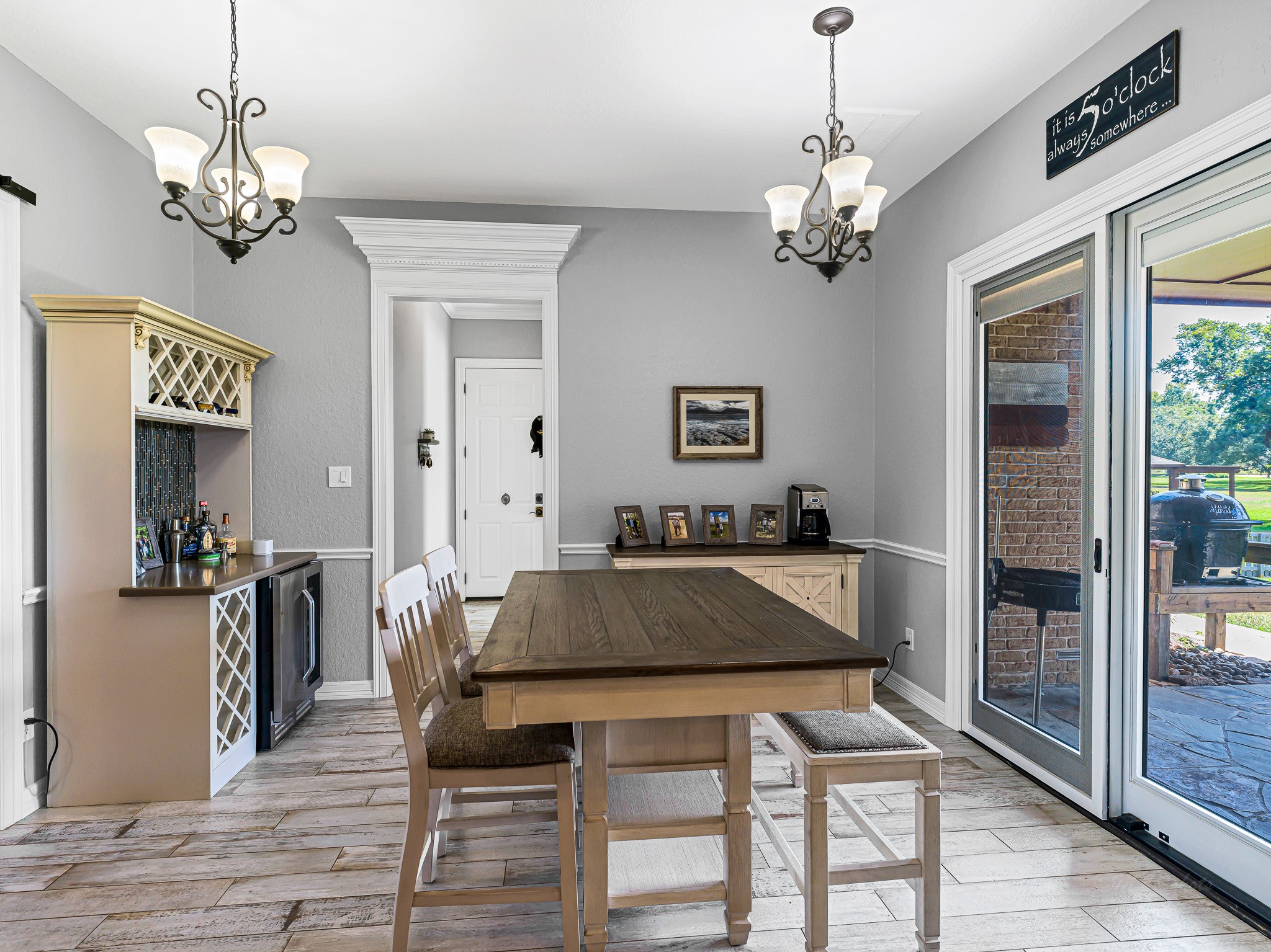 100 Pecan Grove Road Sealy, TX 77474 - Photo 21 of 48 This photo showcases a bright dining area with elegant light fixtures, a wooden table, and chairs. It features sliding glass doors leading to a patio with views of a lush lawn. The space has a modern, inviting feel with neutral walls and wood-style flooring.