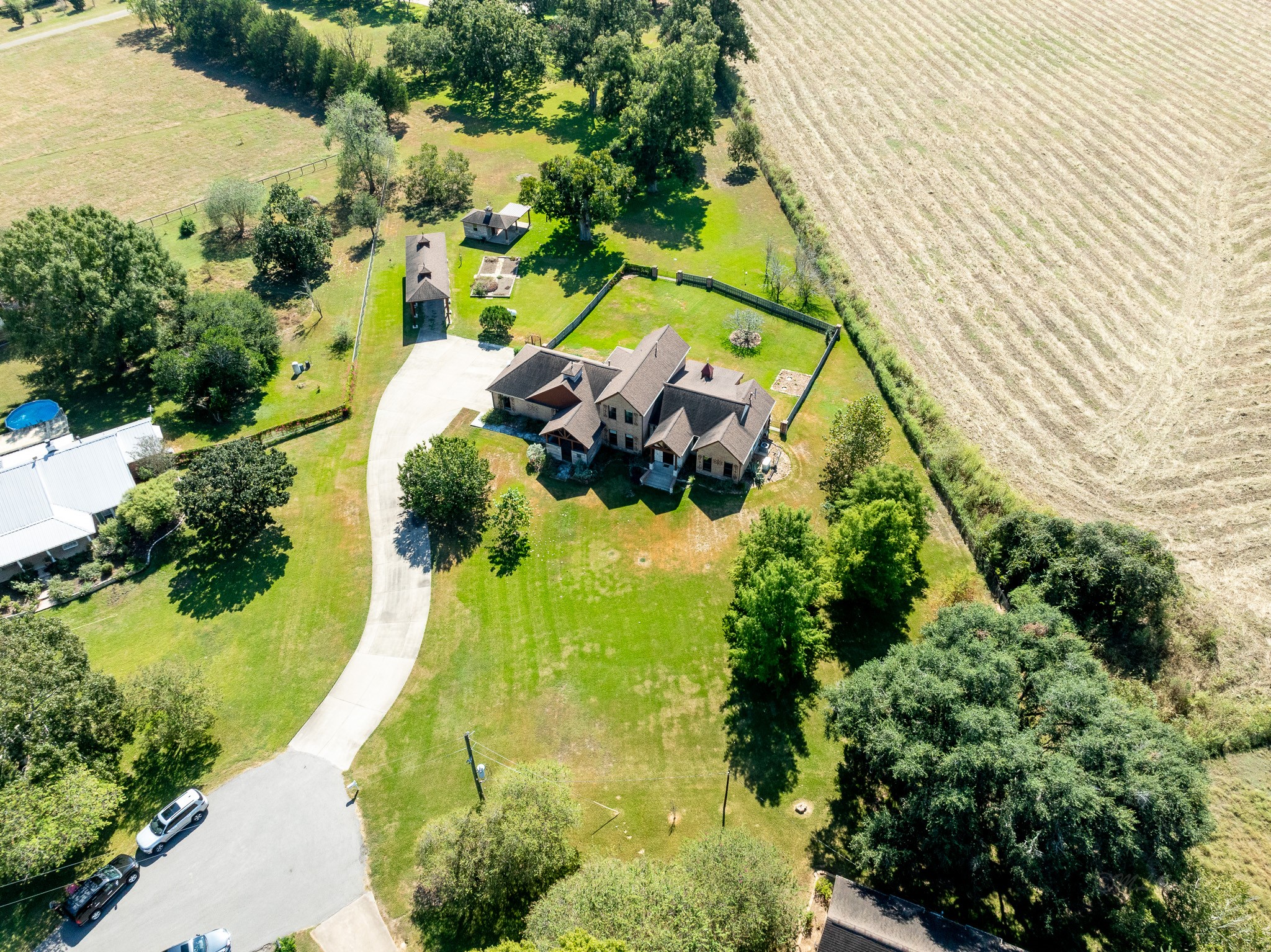 100 Pecan Grove Road Sealy, TX 77474 - Photo 47 of 48 This photo showcases a charming home exterior with a rustic wood facade and a spacious covered patio. The lush green lawn and mature trees provide a serene, scenic backdrop, perfect for outdoor relaxation and entertainment.