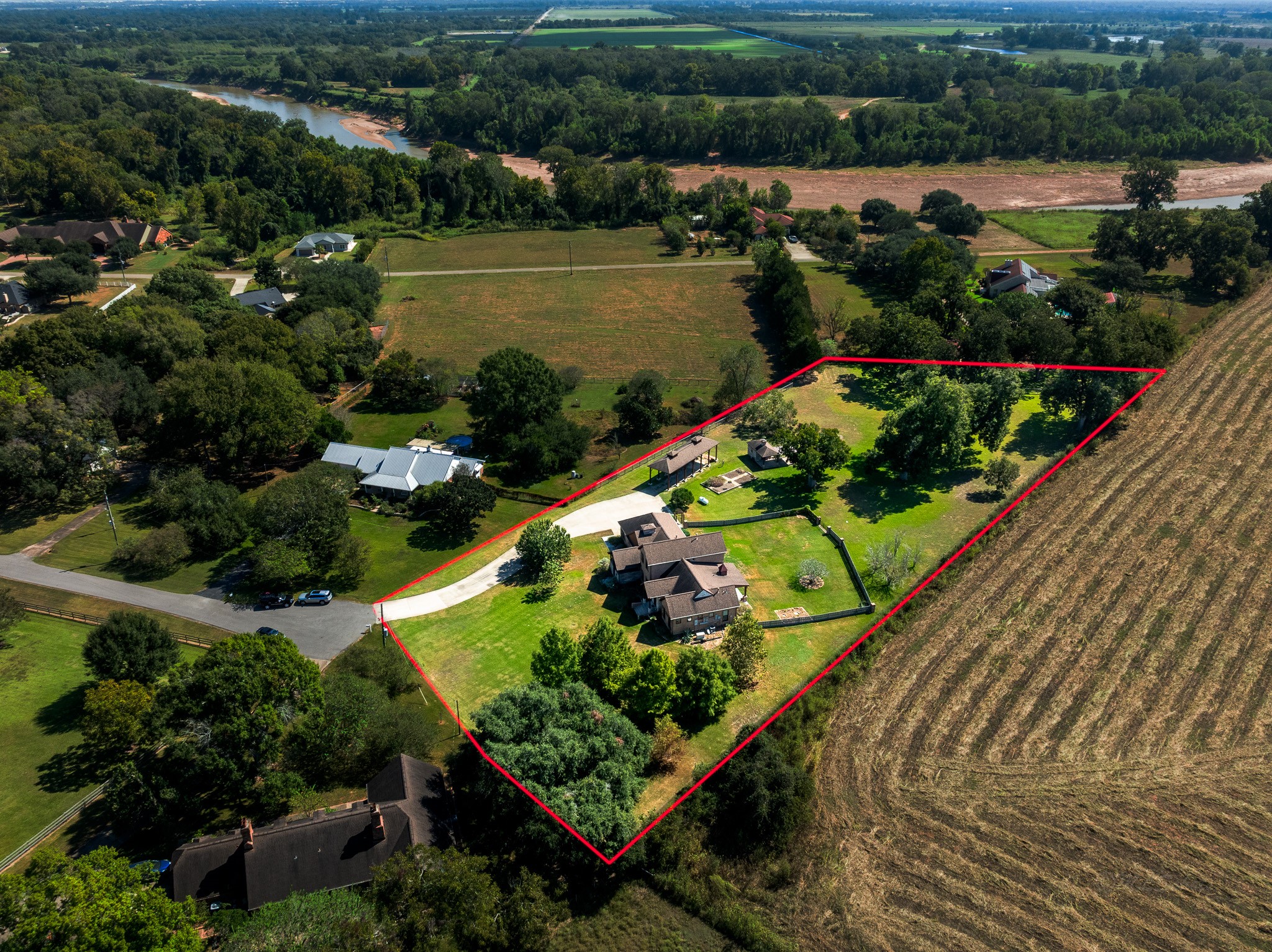 100 Pecan Grove Road Sealy, TX 77474 - Photo 48 of 48 This aerial view showcases a spacious property with a large, elegant house surrounded by lush greenery. The home features a well-maintained yard, a long driveway, and additional outbuildings, all set against a backdrop of open fields and mature trees, offering privacy and a serene country feel.