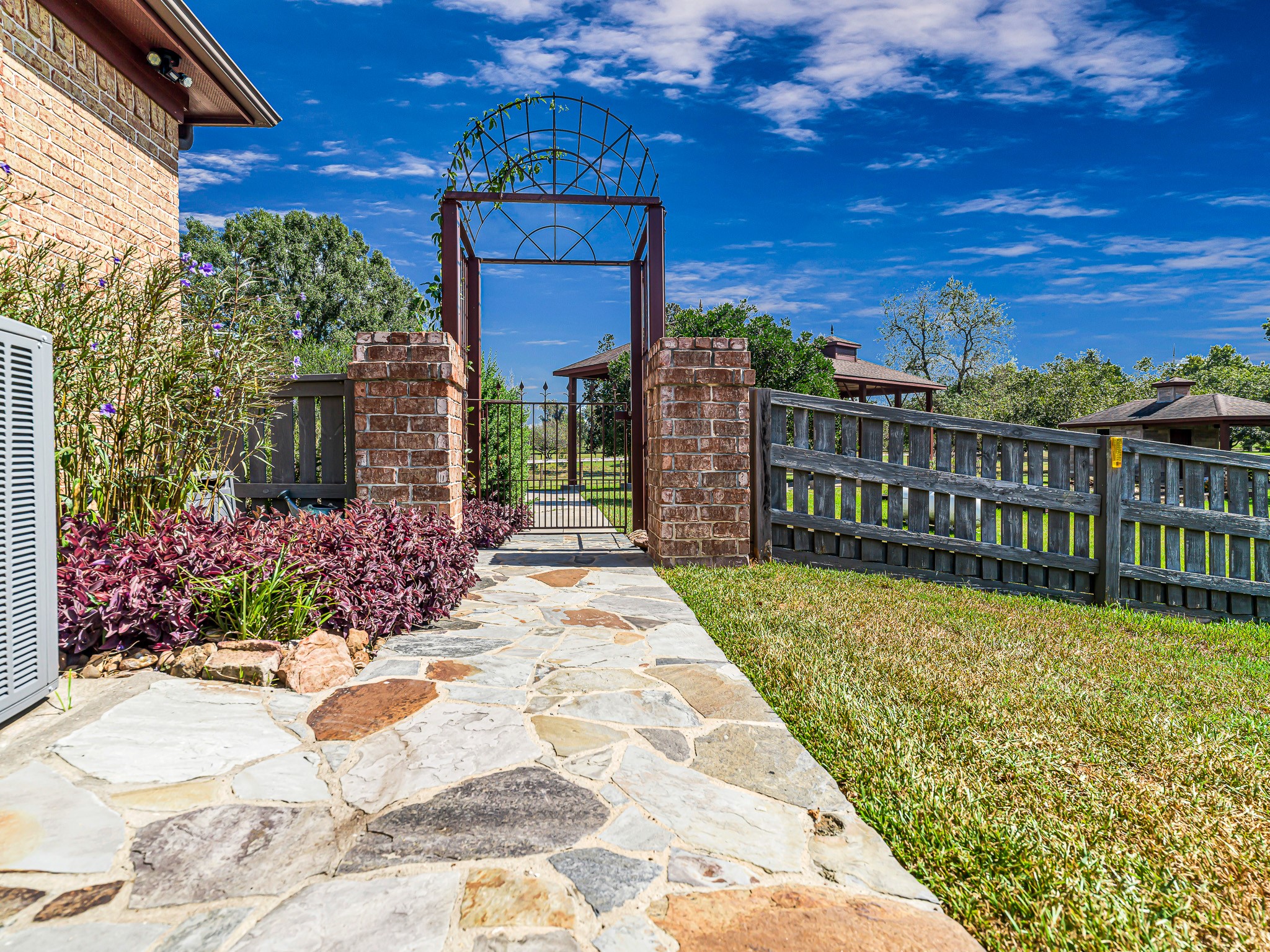 100 Pecan Grove Road Sealy, TX 77474 - Photo 7 of 48 This photo showcases a cozy patio with a rustic stone floor and wood-paneled walls, featuring a decorative metal gate and a view of lush greenery. Perfect for outdoor relaxation.
