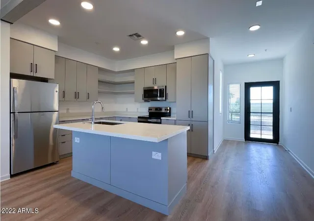 a kitchen with stainless steel appliances granite countertop a refrigerator a sink dishwasher a stove and white countertops with wooden floor