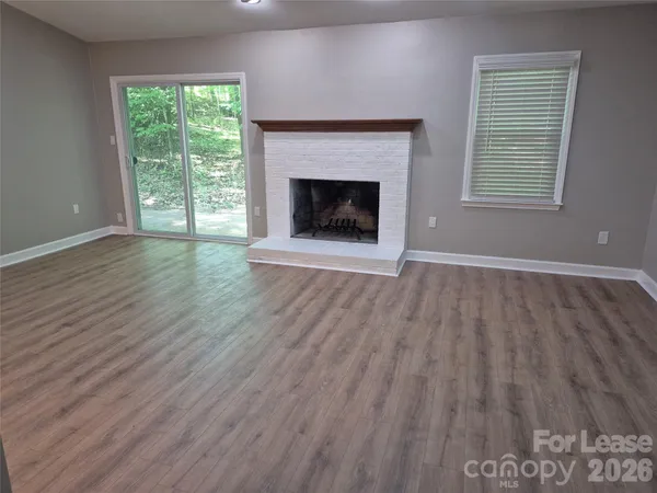 an empty room with wooden floor fireplace and windows
